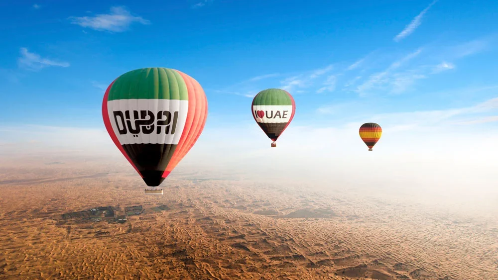 Hot air balloons flying over golden desert dunes at sunrise in Dubai.