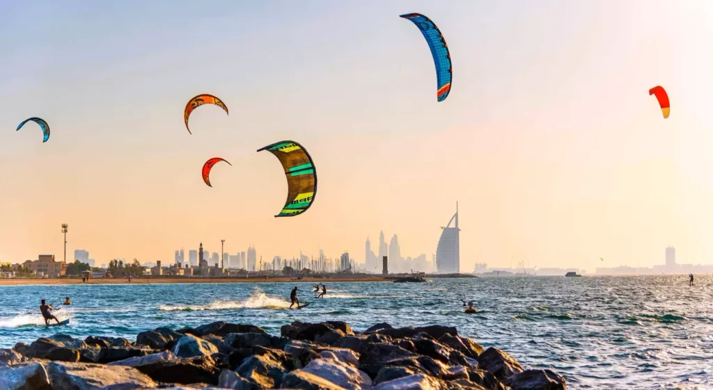 Kite surfers enjoying waves at Kite Beach Dubai with city skyline in background.